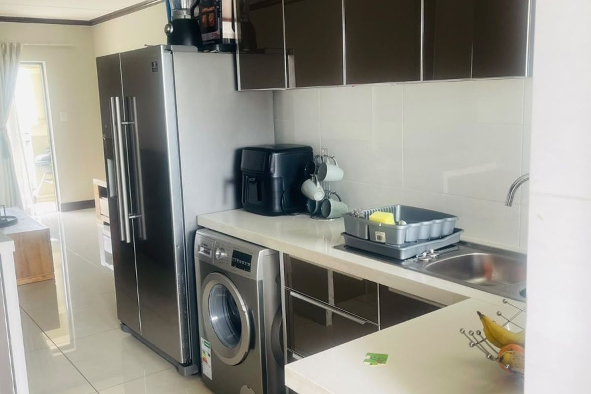 Compact kitchen featuring modern dark cabinetry, white countertops, tiled flooring, and integrated space for laundry appliances.