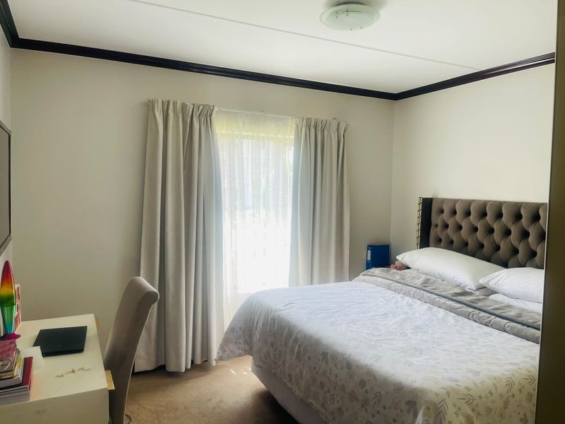 A well-lit bedroom featuring neutral walls, dark crown molding, and a large window with curtains, providing a comfortable and functional living space.