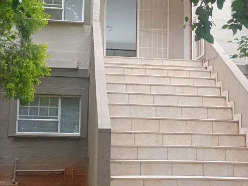 Exterior view of an apartment building entrance featuring a tiled staircase leading to a security gate and ground floor windows.