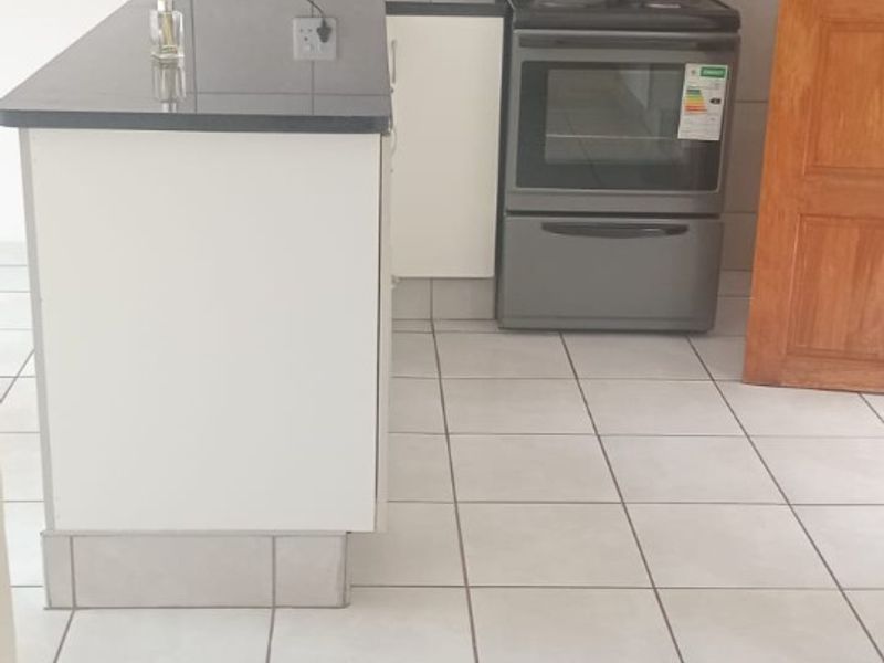 A clean, functional kitchen featuring white cabinetry, dark granite countertops, a freestanding stove, and neutral tiled flooring throughout.