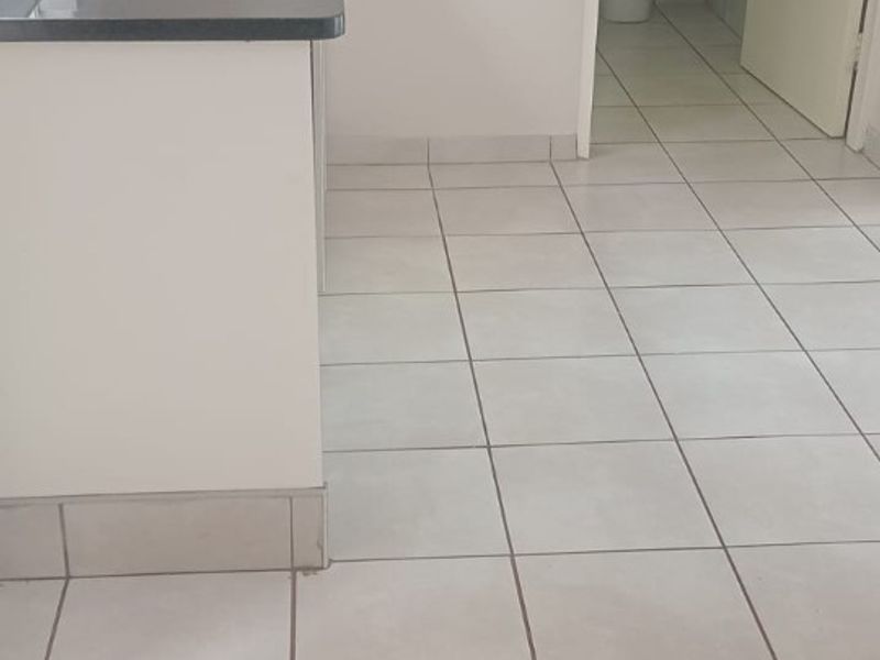 A clean, functional kitchen area featuring a stainless steel sink, granite countertop, and neutral floor tiles, with an adjacent bathroom visible.