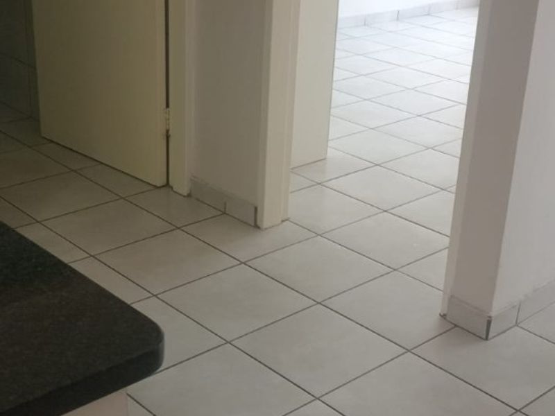 A clean, empty hallway featuring neutral tiled flooring and internal doors, providing a bright and functional transition space within the apartment.
