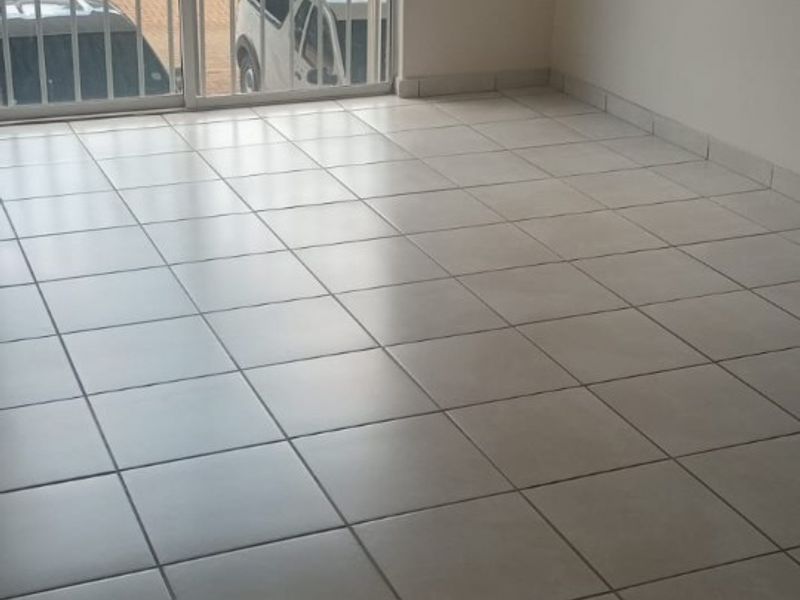 An empty living room featuring neutral tiled flooring and a large sliding glass door leading to a balcony.