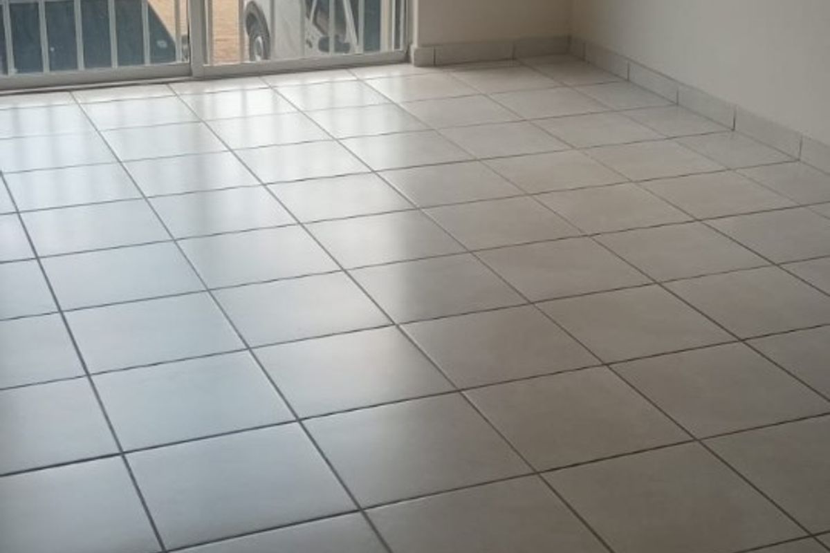 An empty living room featuring neutral tiled flooring and a large sliding glass door leading to a balcony.