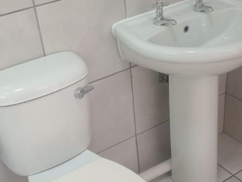 A functional bathroom featuring a pedestal basin with dual-handle taps, a close-coupled toilet, and neutral ceramic wall and floor tiling.