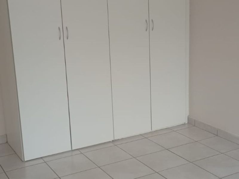 A clean, empty bedroom featuring neutral tiled flooring and white built-in cupboards, offering a blank canvas for personalization.