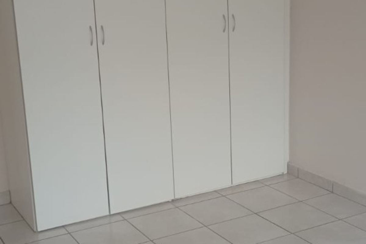 A clean, empty bedroom featuring neutral tiled flooring and white built-in cupboards, offering a blank canvas for personalization.