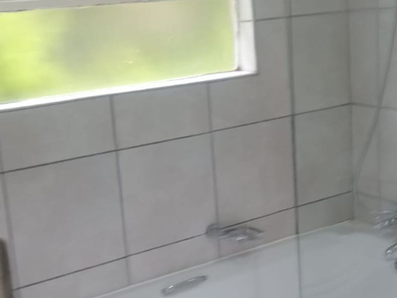 A functional bathroom featuring a bathtub with a glass shower screen, tiled walls, and tiled flooring.