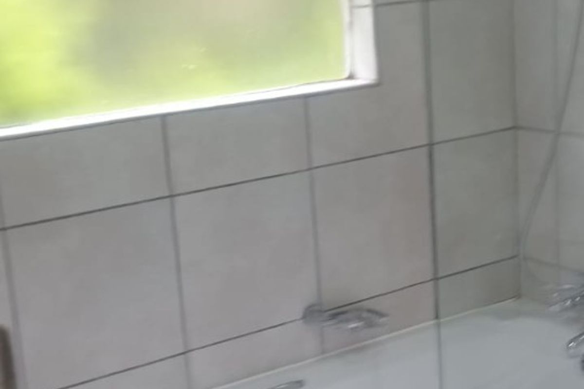 A functional bathroom featuring a bathtub with a glass shower screen, tiled walls, and tiled flooring.