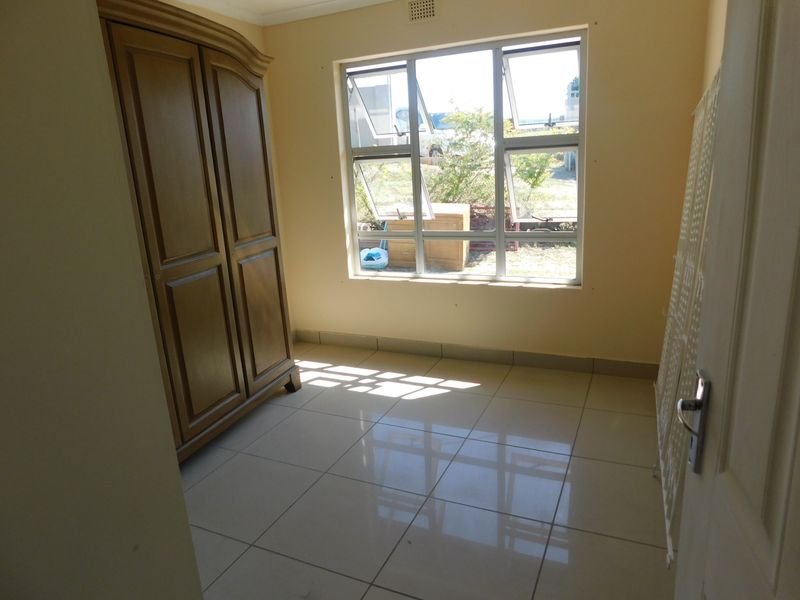 A bedroom featuring neutral tiled flooring and large aluminium-framed windows, providing natural light and a view of the exterior.