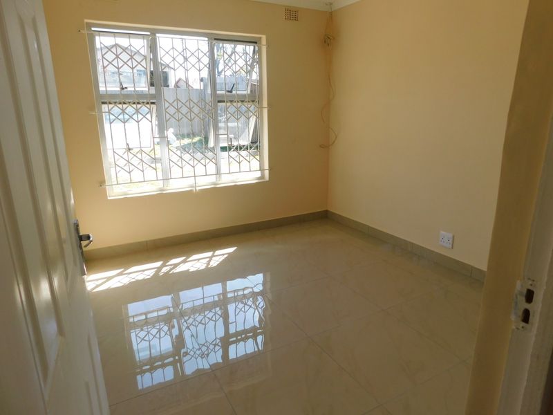 An empty bedroom featuring polished tiled flooring, a window with security bars, and neutral wall paint.