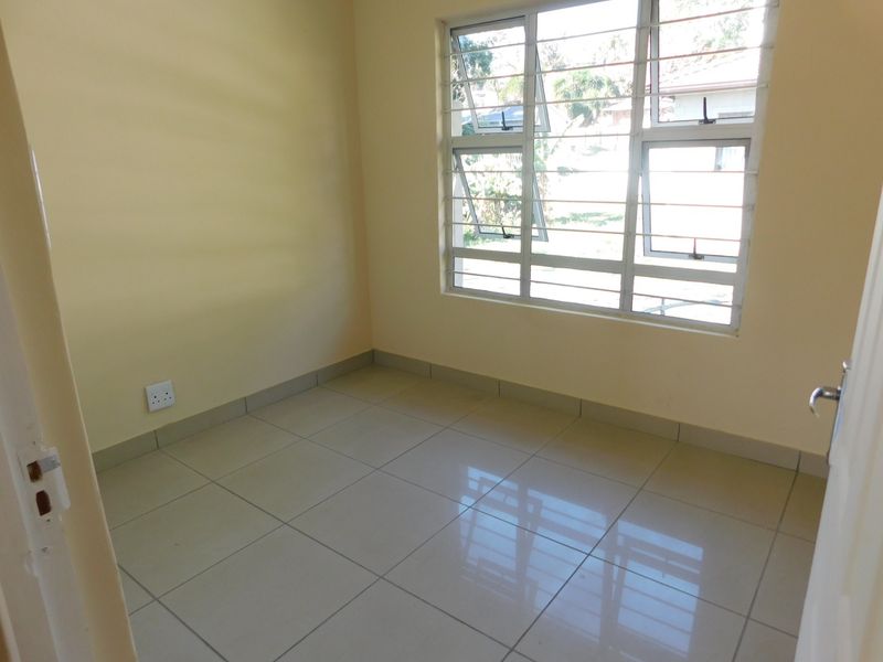 A clean, empty bedroom featuring neutral wall paint, polished floor tiles, and an aluminium window with integrated security bars.