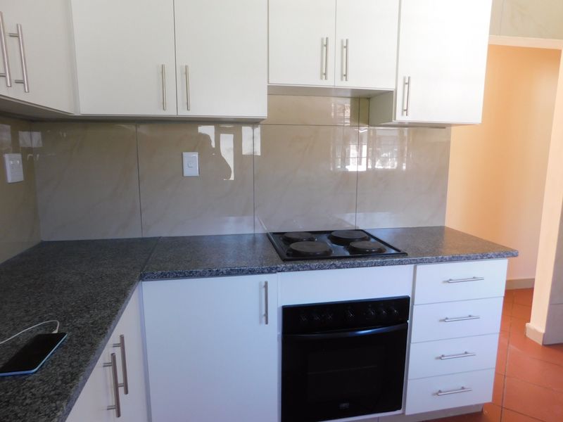 A clean, modern kitchen featuring white cabinetry, granite countertops, and a built-in electric oven and hob with a tiled splashback.