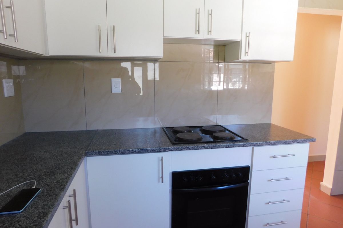 A clean, modern kitchen featuring white cabinetry, granite countertops, and a built-in electric oven and hob with a tiled splashback.