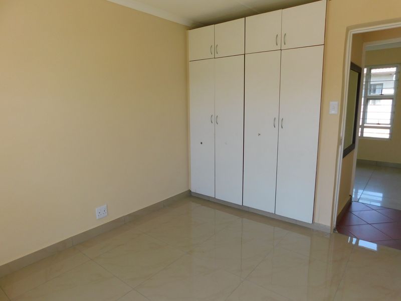 A clean, empty bedroom featuring neutral wall paint, tiled flooring, and ample built-in cupboard storage space.