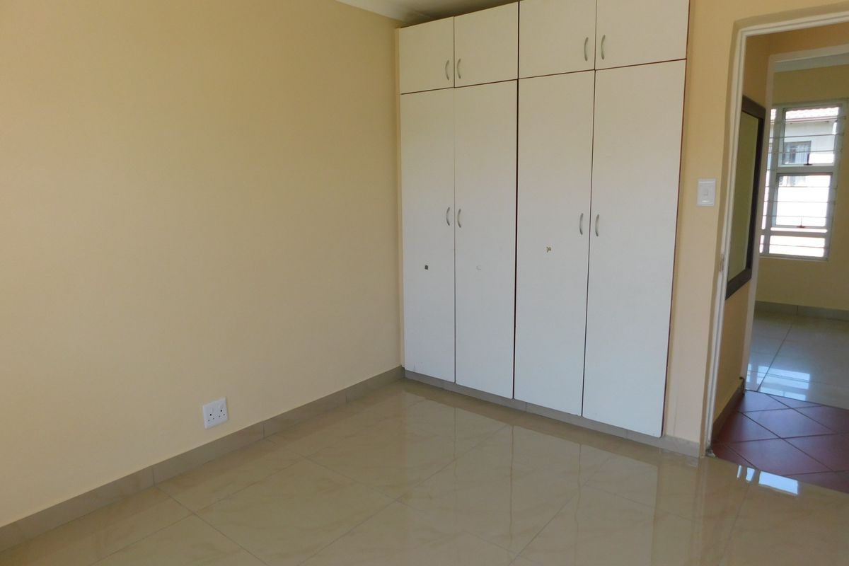 A clean, empty bedroom featuring neutral wall paint, tiled flooring, and ample built-in cupboard storage space.