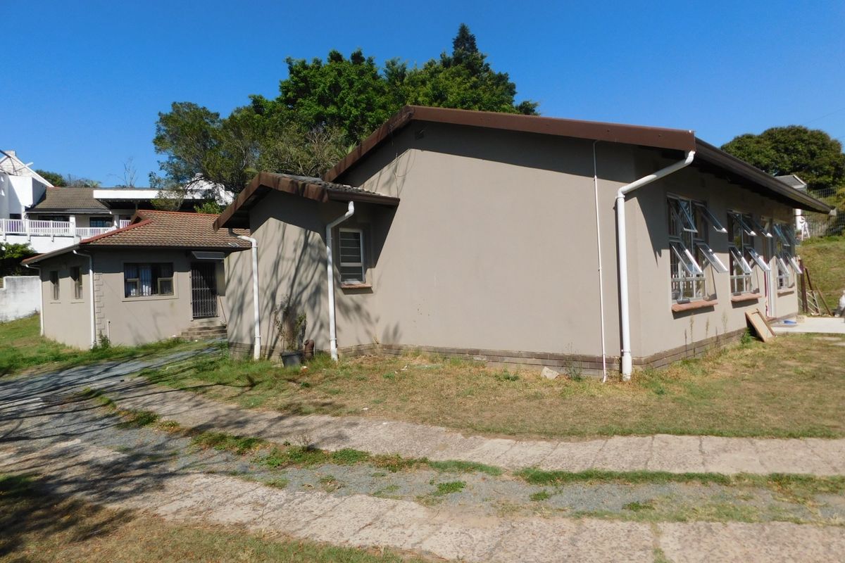 Rear view of a single-story house featuring a tiled roof, aluminium windows, and a paved walkway leading to the building entrance.