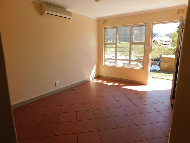An empty living room featuring tiled flooring, a wall-mounted air conditioning unit, and direct access to the exterior through a glass door.