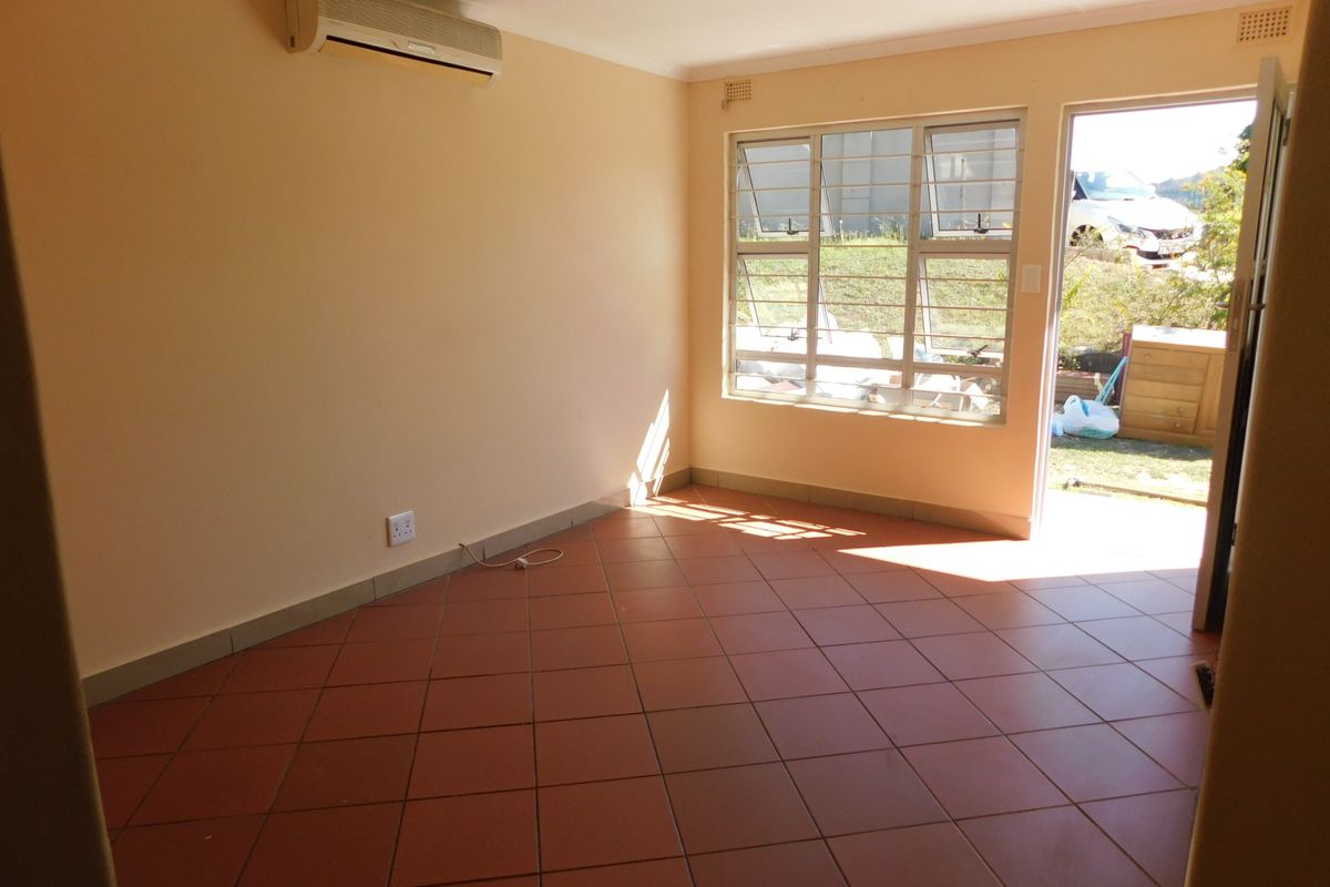 An empty living room featuring tiled flooring, a wall-mounted air conditioning unit, and direct access to the exterior through a glass door.