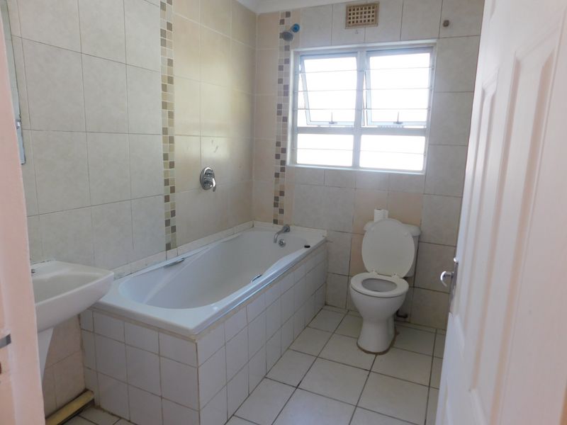 A functional bathroom featuring a built-in bathtub, pedestal basin, and toilet with neutral tiled finishes throughout.