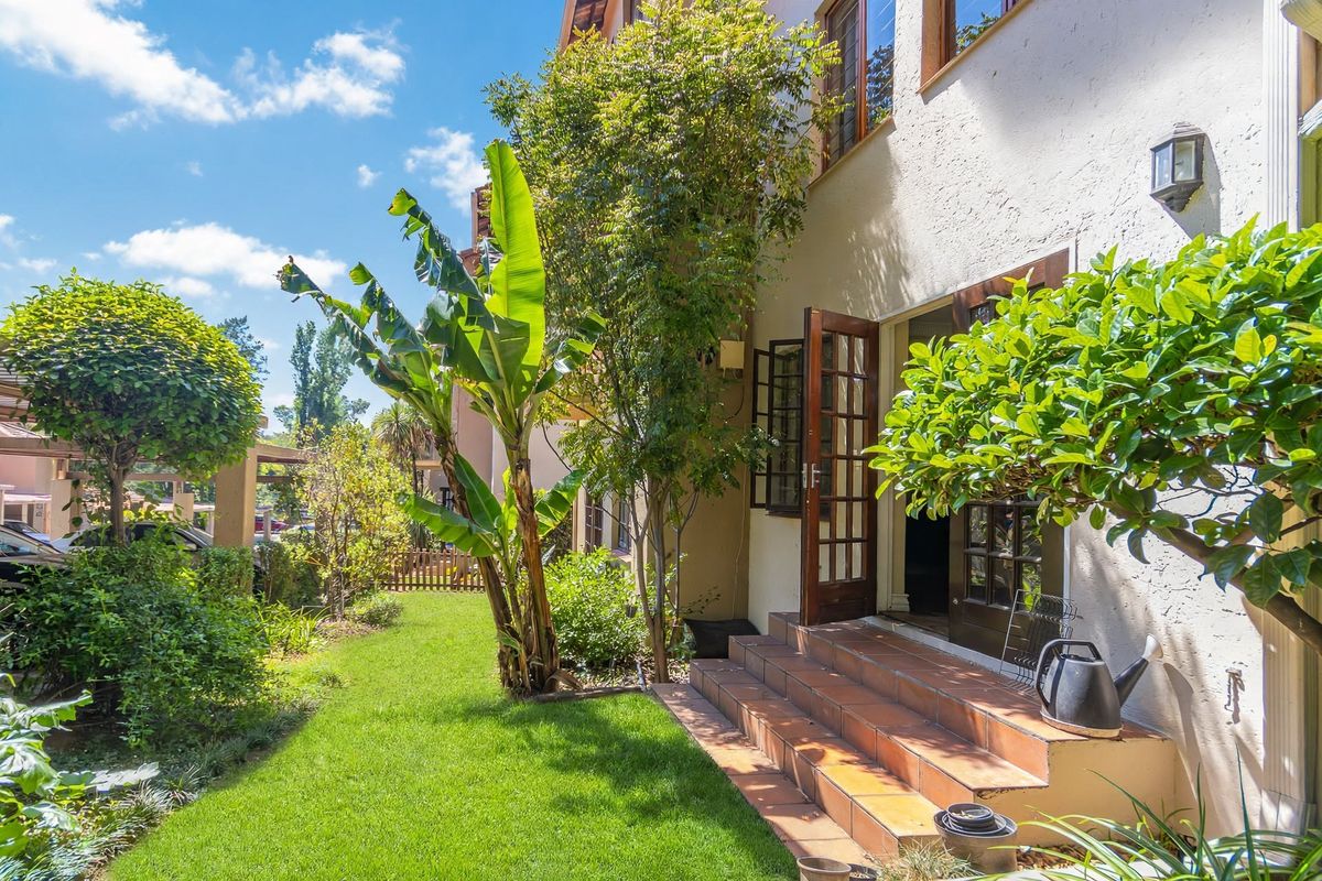 A well-maintained rear garden area featuring tiled steps leading to wooden french doors, surrounded by established greenery and a manicured lawn.