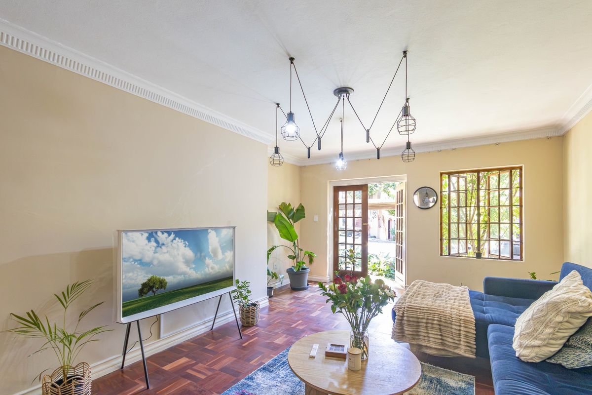 A bright living room featuring classic parquet flooring, elegant crown molding, and large multi-pane windows that provide natural light and access to the exterior.