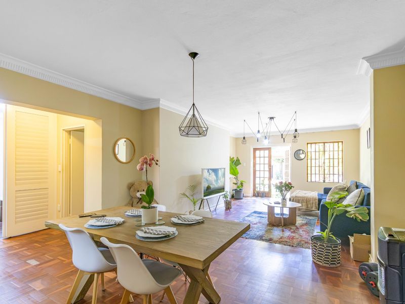 Spacious open-plan living and dining area featuring warm parquet flooring, elegant crown molding, and abundant natural light flowing through to the rear entrance.