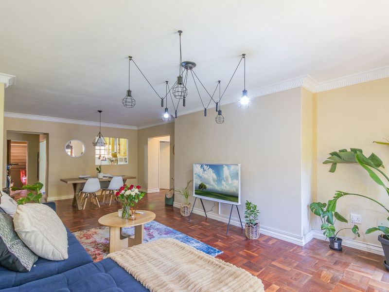 Spacious open-plan living and dining area featuring classic parquet flooring, elegant crown molding, and modern pendant lighting fixtures.