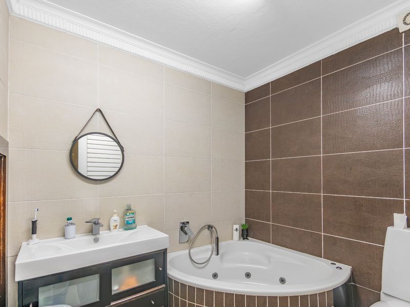 A well-maintained bathroom featuring a corner spa bath, modern vanity unit, and contrasting wall tiling with decorative ceiling cornice.