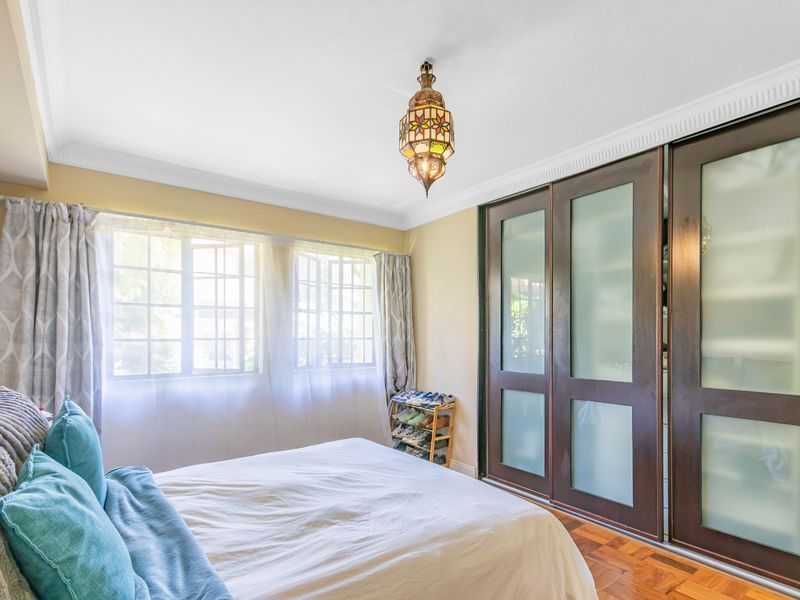 A well-lit bedroom featuring parquet flooring, decorative cornice, and large built-in cupboards with frosted glass sliding doors.