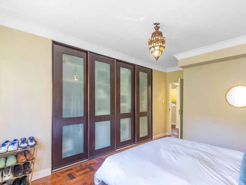 A well-maintained bedroom featuring dark wood built-in wardrobes with frosted glass panels, classic parquet flooring, and decorative crown molding.