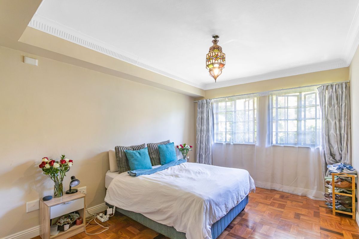 A well-lit bedroom featuring classic parquet flooring, decorative ceiling cornicing, and large casement windows that provide ample natural light.