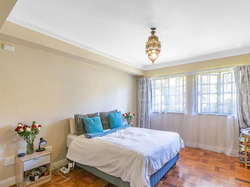 A well-lit bedroom featuring classic parquet flooring, decorative ceiling cornicing, and large casement windows that provide ample natural light.