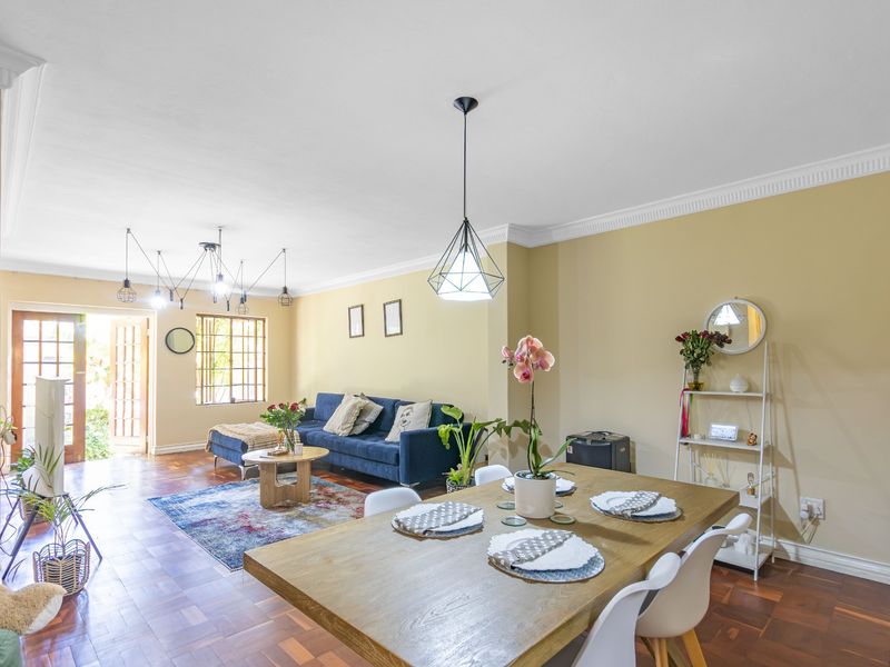 Spacious open-plan living and dining area featuring warm parquet flooring, elegant crown molding, and natural light flowing through classic french doors.
