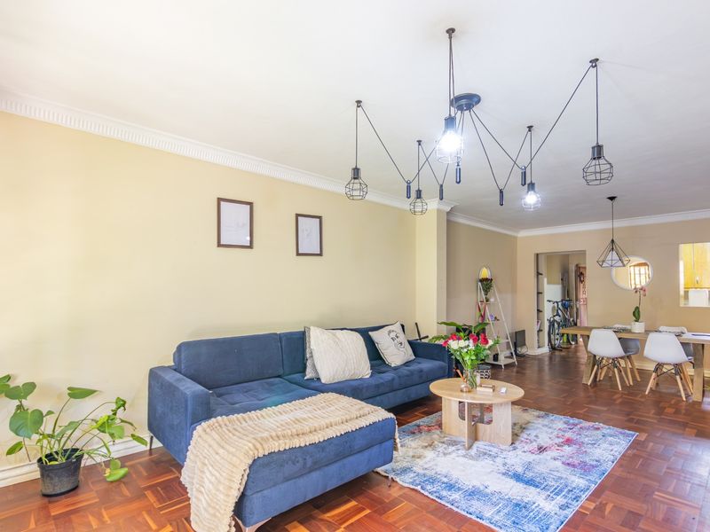 Spacious open-plan living and dining area featuring warm parquet flooring, decorative crown molding, and modern industrial-style pendant lighting.