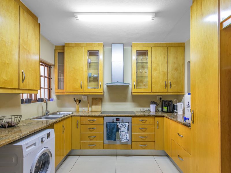 A functional U-shaped kitchen featuring light wood cabinetry, granite countertops, integrated oven and hob, and a dedicated space for a washing machine.