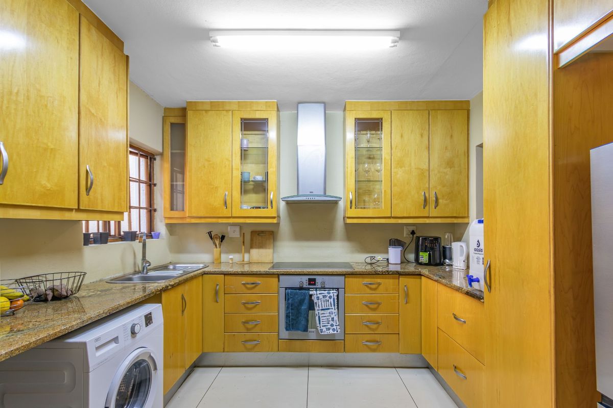 A functional U-shaped kitchen featuring light wood cabinetry, granite countertops, integrated oven and hob, and a dedicated space for a washing machine.