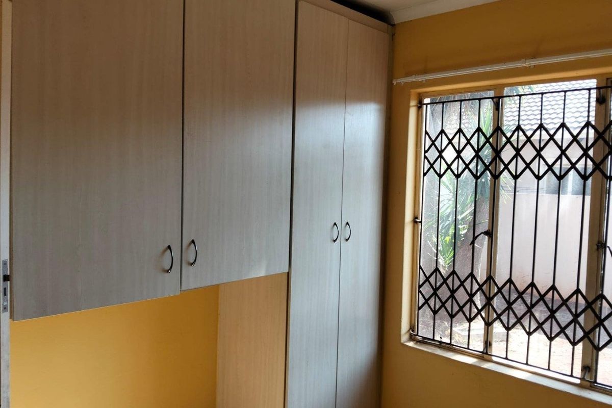 A bedroom featuring built-in cupboards and a window fitted with a security gate.