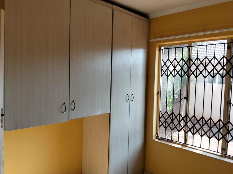 A bedroom featuring built-in cupboards and a window fitted with a security gate.