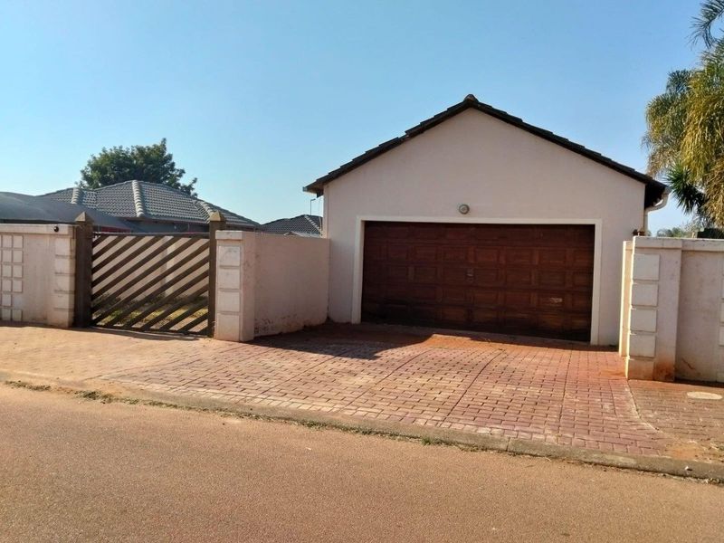 Front exterior view of the property featuring a single garage with a paved driveway and secure boundary wall with a pedestrian gate.