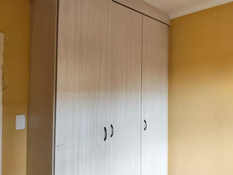 A bedroom featuring a light wood-finish built-in wardrobe against yellow painted walls.