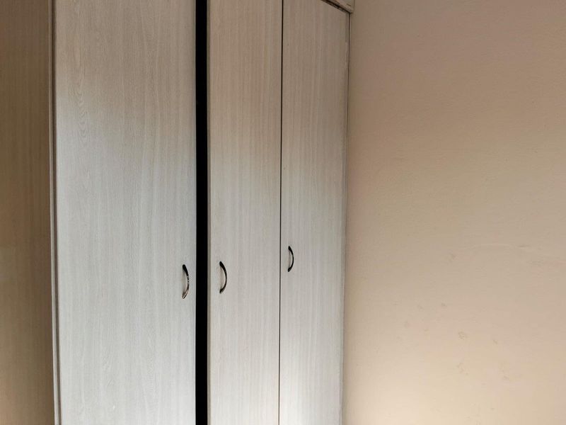 A bedroom interior featuring a light wood-finish built-in wardrobe against a plain wall.