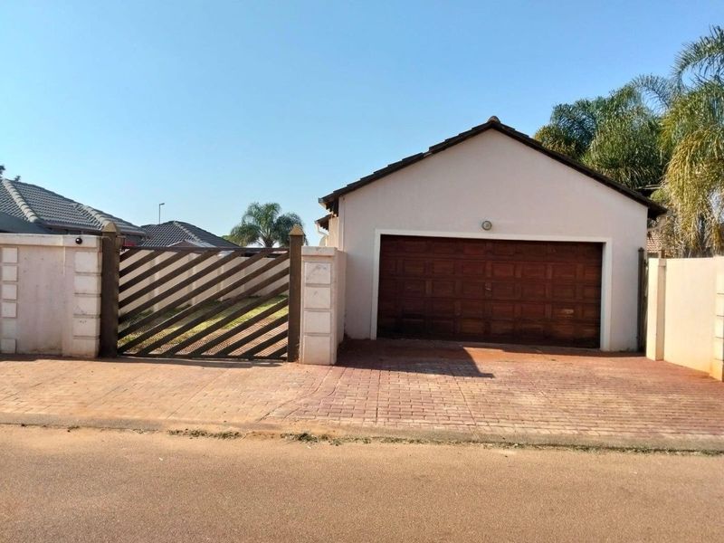 Front view of the property featuring a single garage with a wooden door, paved driveway, and a secure gated entrance with boundary walls.