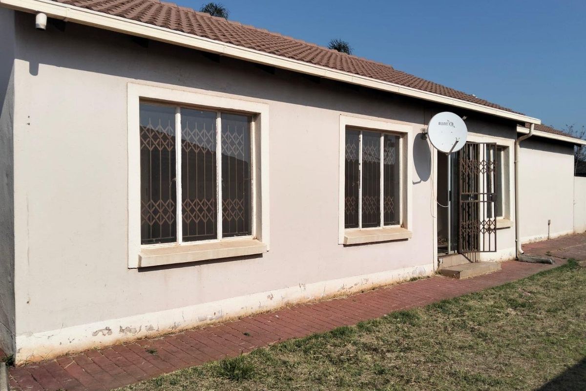 Rear exterior view of the house featuring a tiled roof, security bars on windows, a security gate, and a paved walkway along the building perimeter.