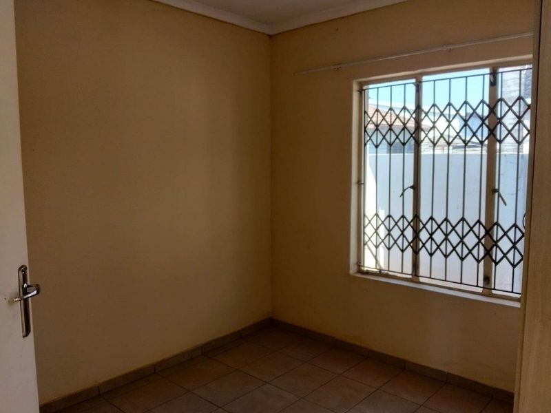 An empty bedroom featuring tiled flooring and a window fitted with a security gate.