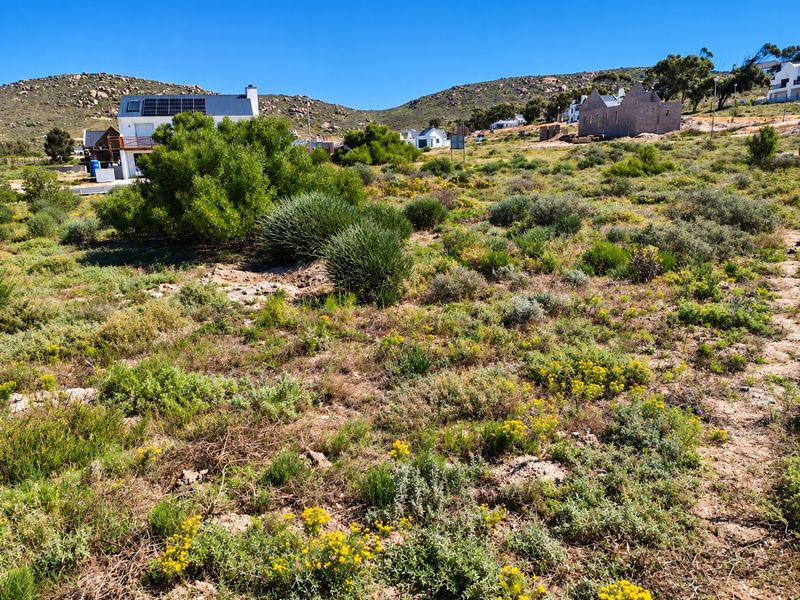 A view of a vacant residential plot featuring natural vegetation and surrounding hillside landscape in a quiet coastal estate.