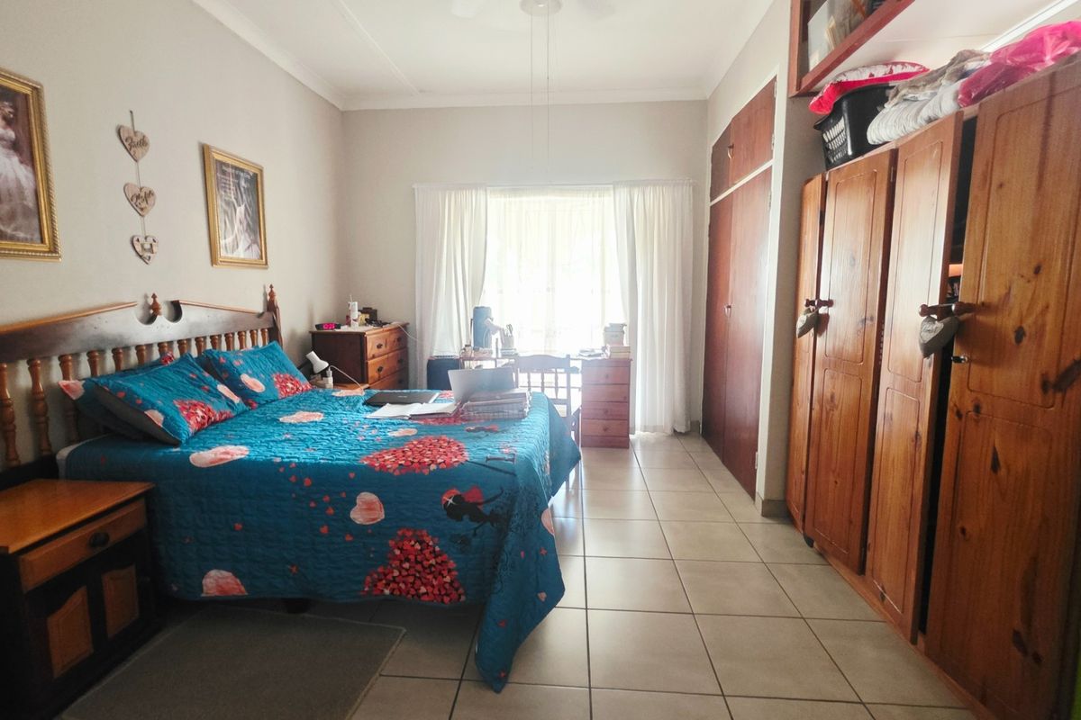 A spacious bedroom featuring tiled flooring, built-in wooden cupboards, and a ceiling fan, offering a functional layout with natural light.