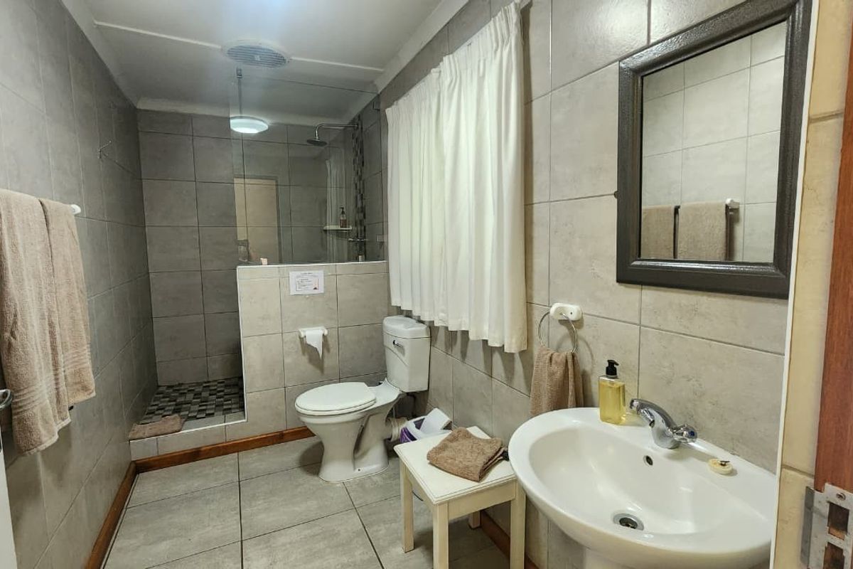 A functional bathroom featuring a walk-in shower with glass screen, pedestal basin, toilet, and neutral floor-to-ceiling wall tiling.