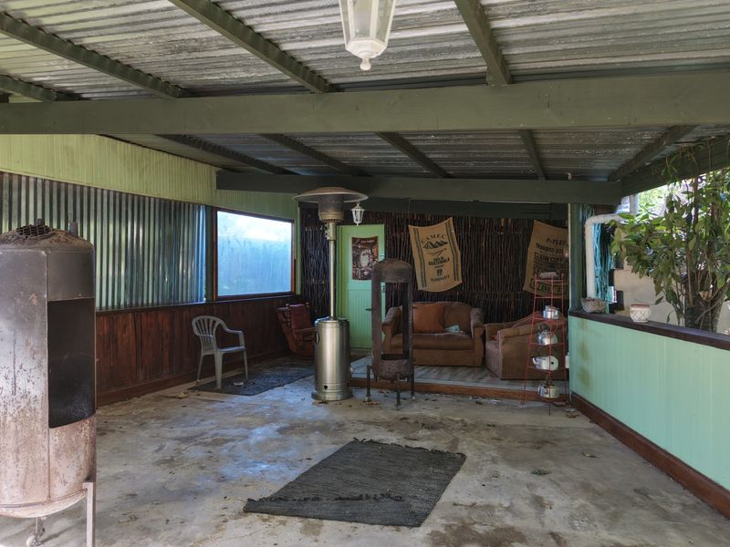 A covered outdoor patio area featuring corrugated metal roofing, timber wall paneling, and concrete flooring, offering a rustic space for outdoor relaxation.