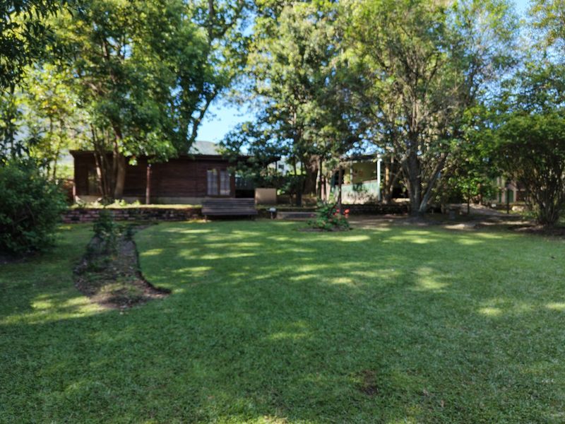 A spacious, tree-lined garden area featuring a well-maintained lawn and a low retaining wall, providing a private outdoor setting.